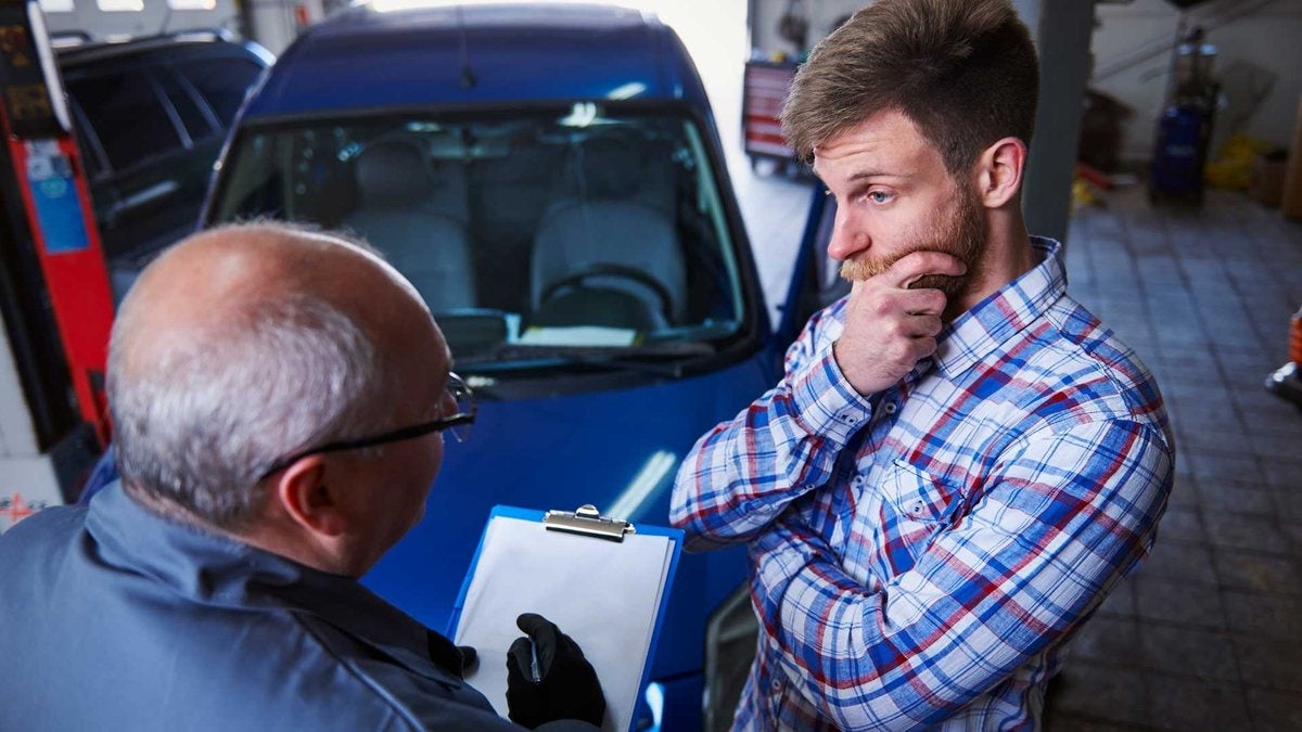 Appraiser with a clipboard reviewing a blue car with its owner during a trade-in appraisal